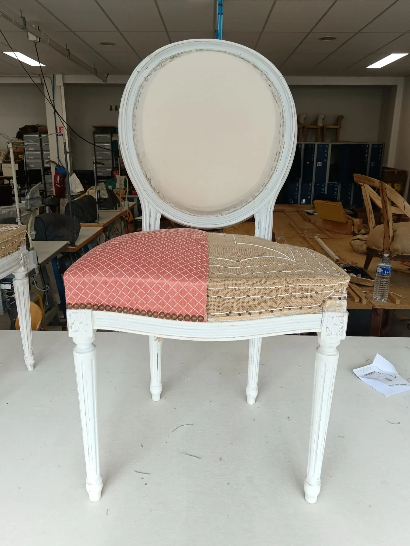 Chaise de style Louis XVI patinée, dont une moitié de l’assise laisse voir la garniture traditionnelle et l’autre le tissu rose bordé de clous décoratifs