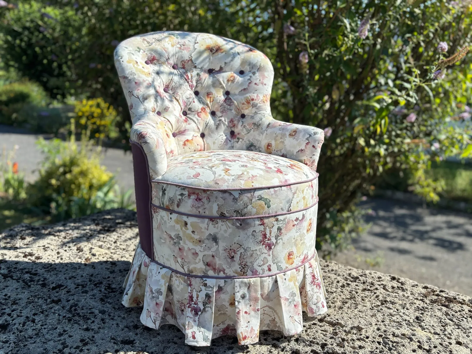 Chauffeuse capitonnée recouverte d’un tissu d’inspiration aquarelle, photographiée au jardin