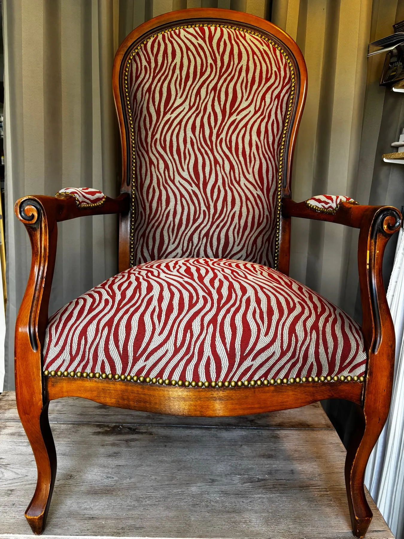 Fauteuil Voltaire en bois fruitier habillé d’un tissu à motifs rouge et écru, orné de clous décoratifs