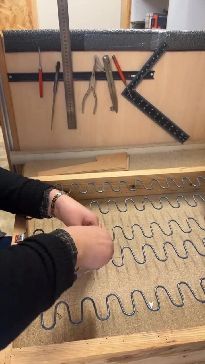 Mains laçant à la ficelle une série de ressorts nozags sur un bâti de banquette