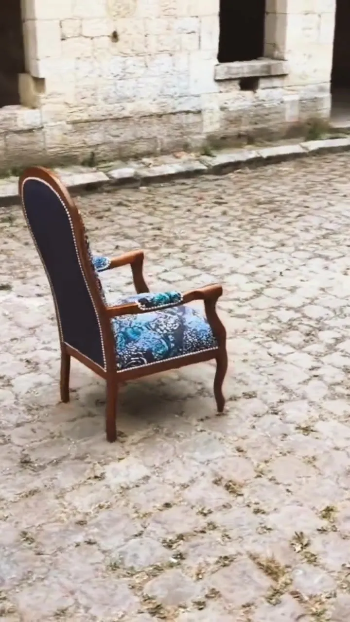 Fauteuil Voltaire habillé d’un imprimé bleu et écru, posé sous la voûte de pierre d’un site ancien
