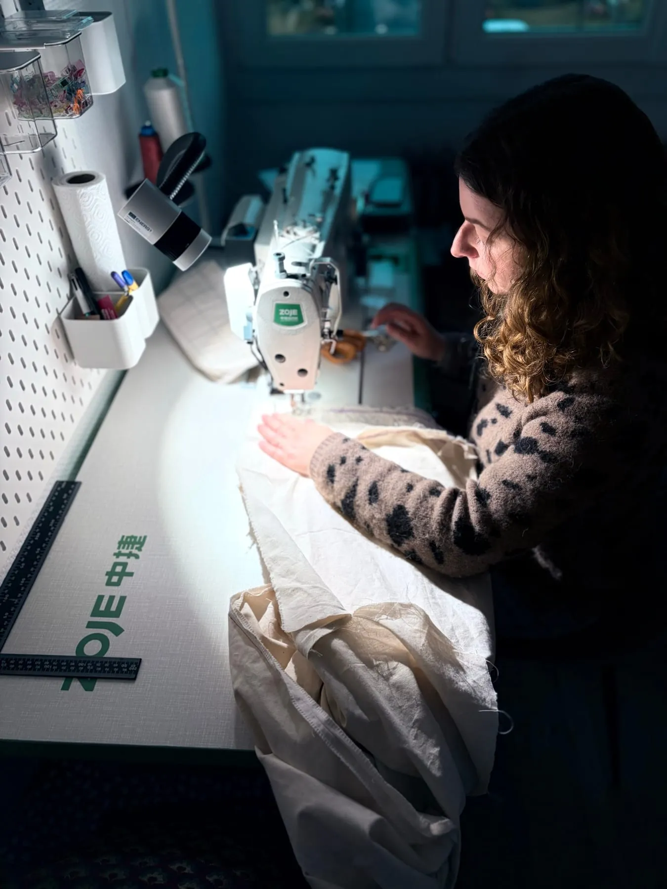 Perrine Wisniewski à la machine à coudre, dans la lumière de l’atelier