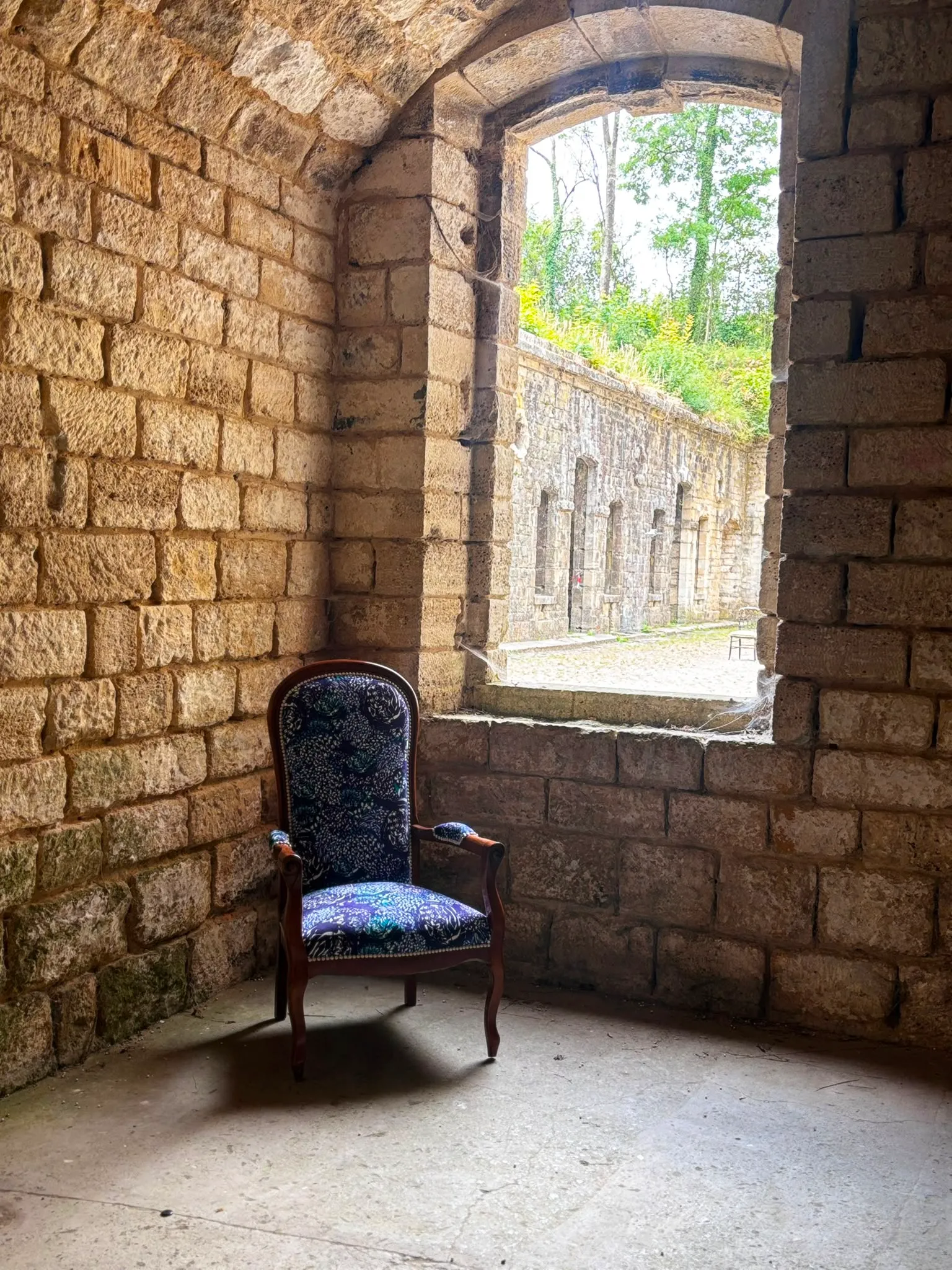 Le fauteuil Voltaire bleu posé dans une salle voûtée, près d’une ouverture en pierre